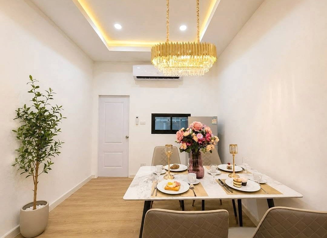 Bright dining room with a marble table set for four, a floral centerpiece, and a gold chandelier.