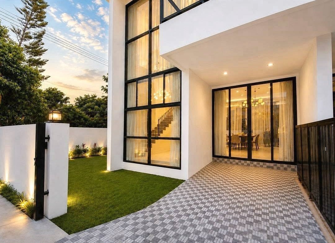 Modern white house with large black-framed glass doors and a tiled entry, illuminated at dusk.