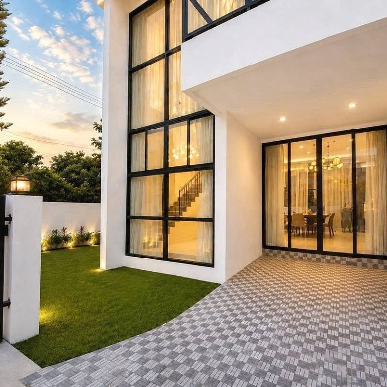 Modern white house with large black framed glass doors and a tiled entry illuminated at dusk