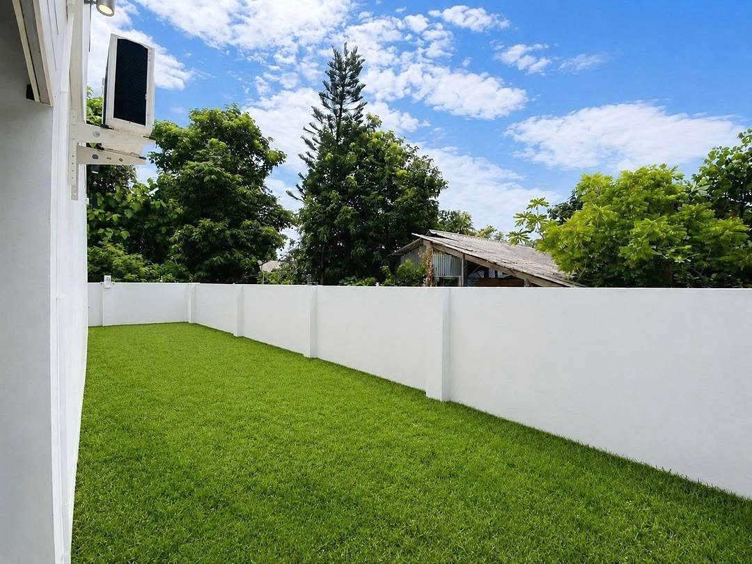 Deperfect_Village_a1_Rdl365_20 Backyard with a bright green lawn, white privacy fence, and a blue sky with clouds; an outdoor AC unit is mounted on the house wall to the left.