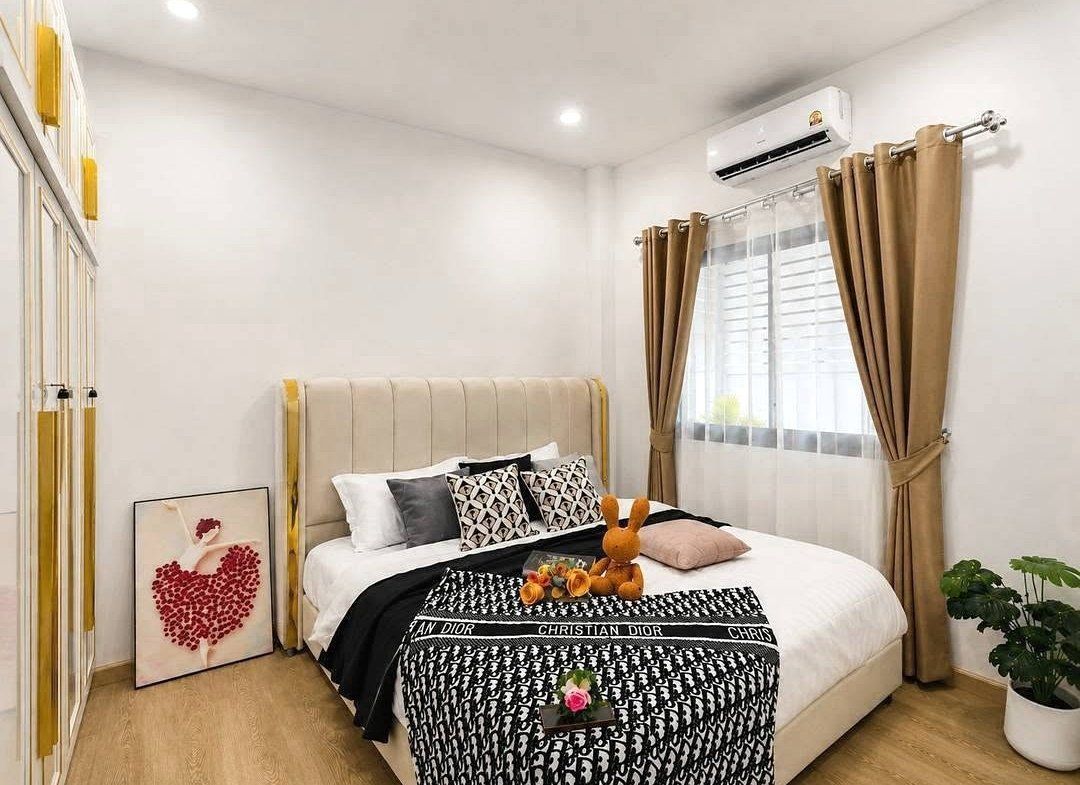 Modern bedroom with beige upholstered bed, black-and-white Dior blanket, and decorative pillows; stuffed orange bunny on bed.