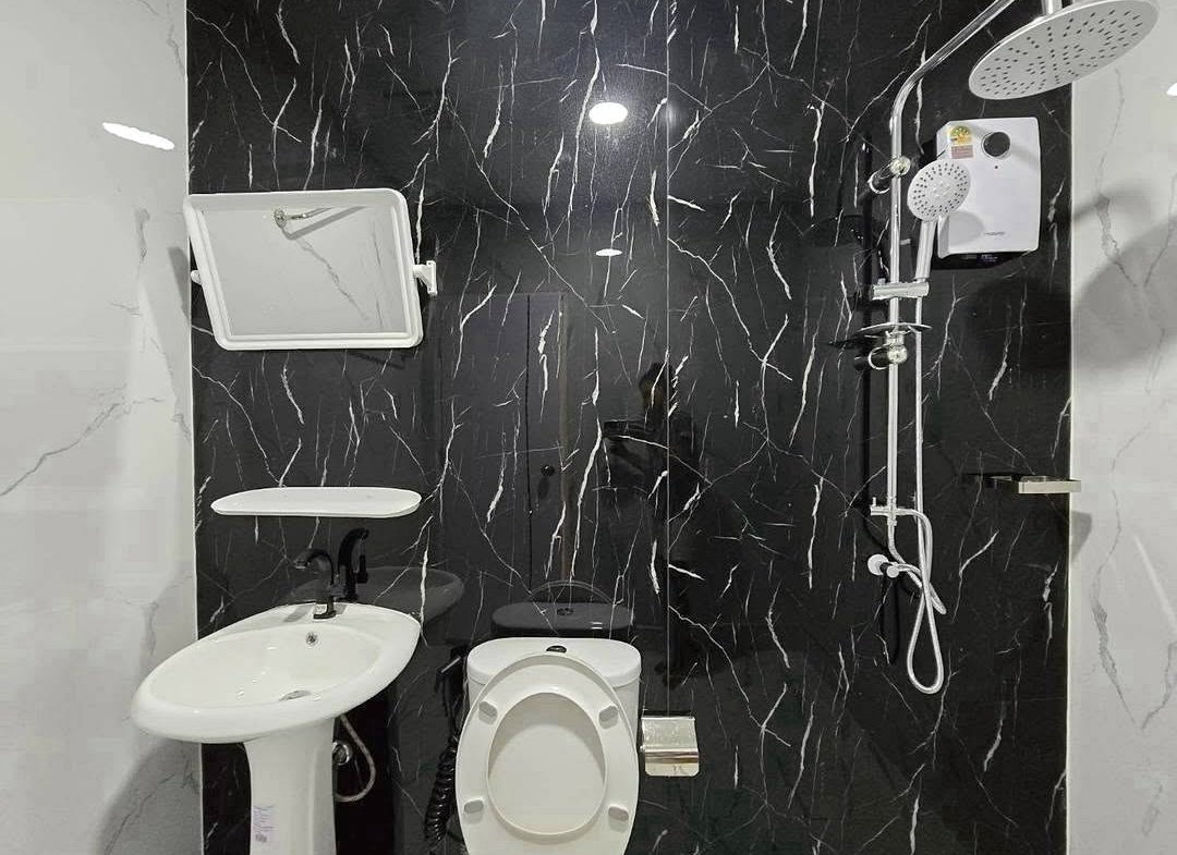 Compact bathroom with a white toilet, pedestal sink, and wall-mounted mirror on black marble walls, plus a modern shower system on the right.