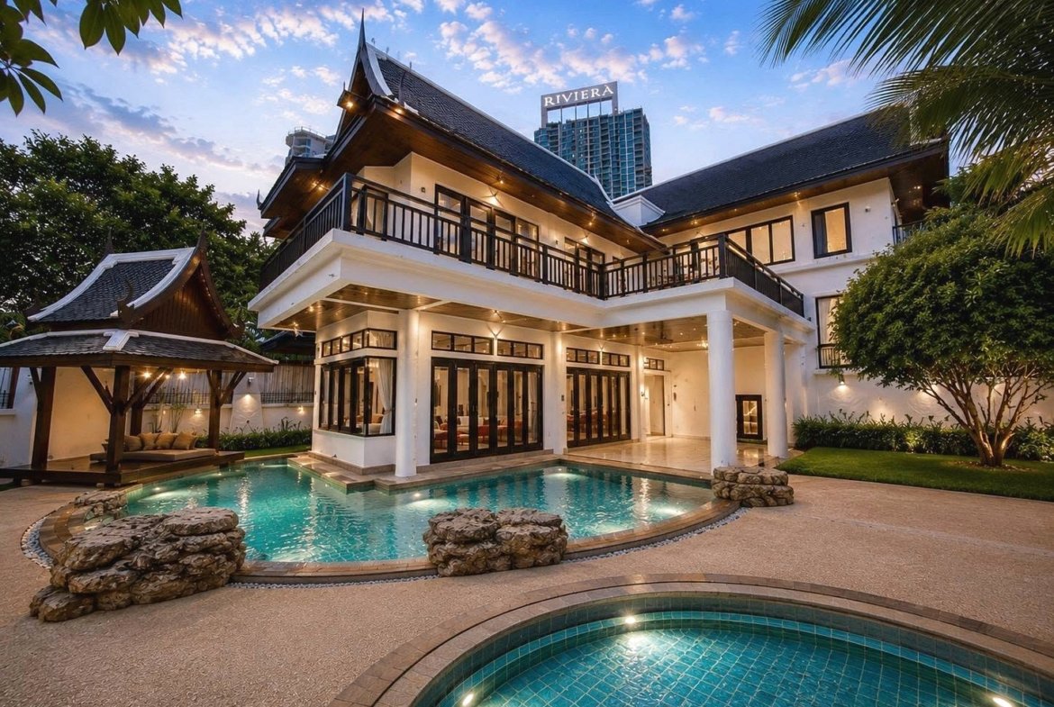 Two-story resort villa with dark wooden railings, large glass doors, and a turquoise pool in a tropical setting.