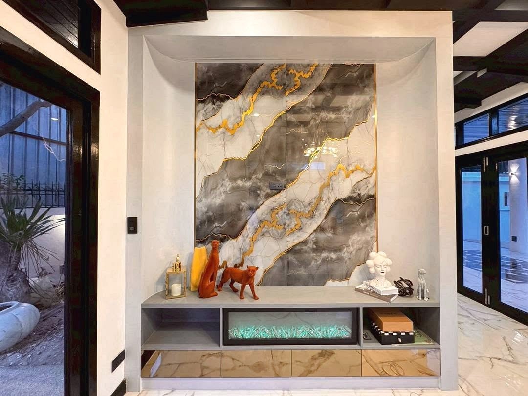 Dharawadi_Poolvilla_Rent_Rdl353_13 A modern entryway with a large marble wall panel featuring gold veining above a gray console cabinet displaying orange animal sculptures, a white bust, books, and decorative objects, with teal backlighting in the bottom drawer.