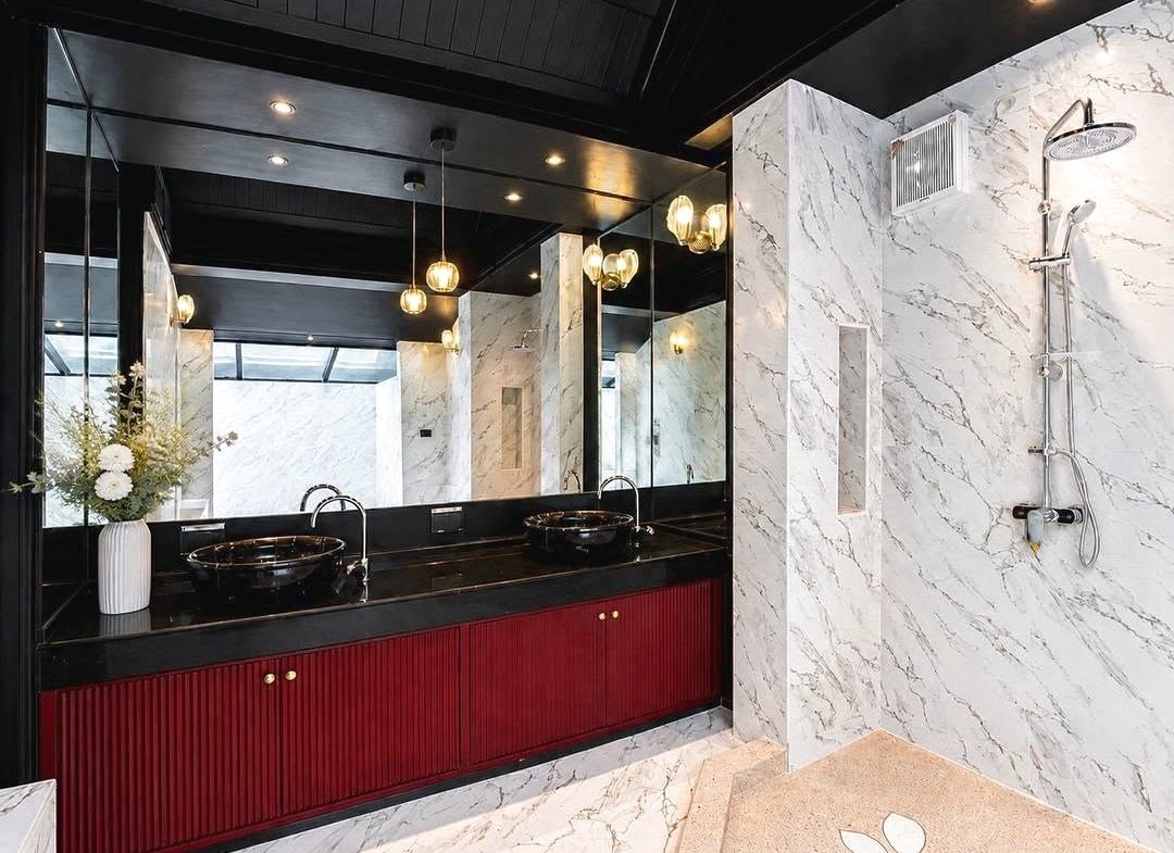 Luxurious marble bathroom with a dual-sink vanity, black countertop, and red cabinetry next to a glass-enclosed shower.