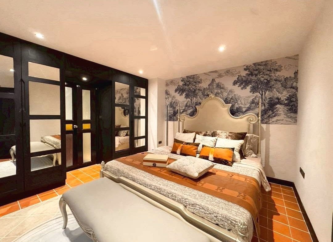 Luxurious bedroom with an ornate upholstered bed, black-framed wardrobes, and a tree mural wall behind the headboard.