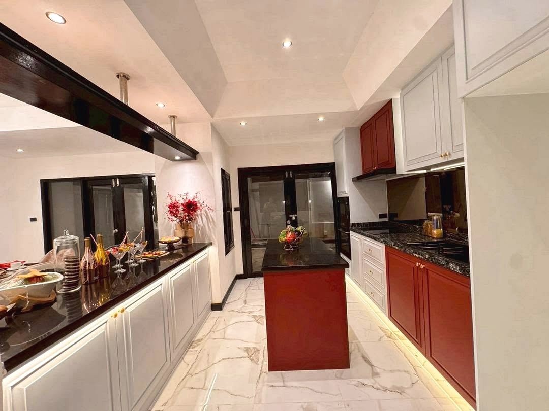 Dharawadi_Poolvilla_Rent_Rdl353_26 Modern L-shaped kitchen with white upper cabinets, red lower cabinets, and a central island on a marble floor; warm under-cabinet lighting and a beverage setup on the left counter.
