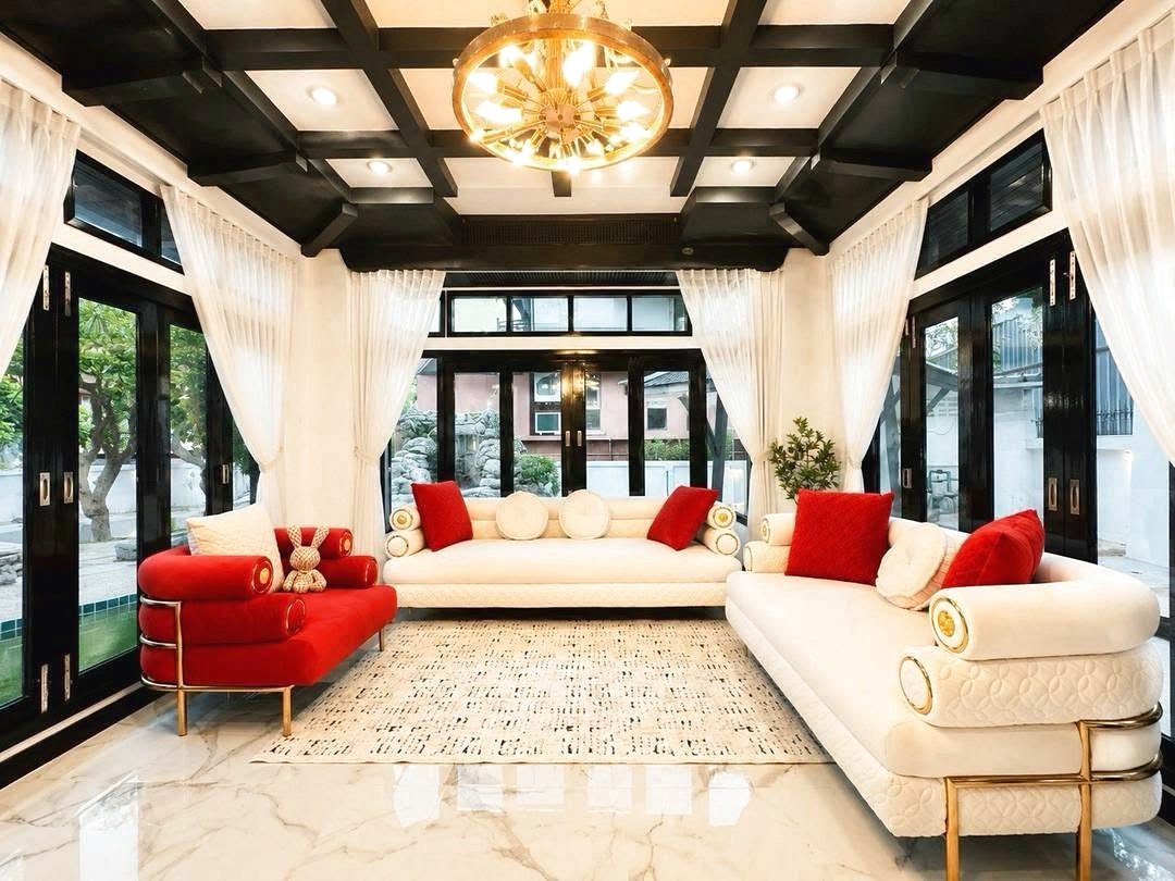 Dharawadi_Poolvilla_Rent_Rdl353_3 Bright, modern living room with white sofas, red cushions, black ceiling beams, and a gold chandelier at the center.