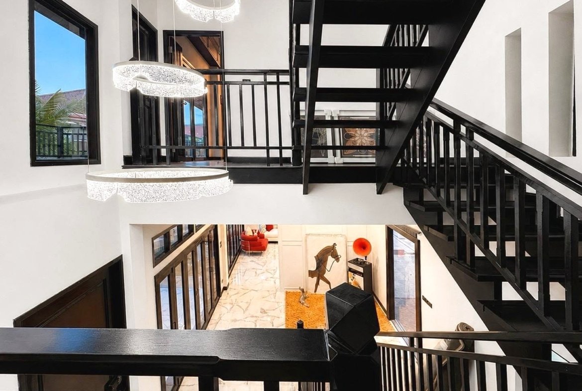 Interior view of a modern multi-level foyer with a black metal staircase, white walls, and circular pendant lights above.