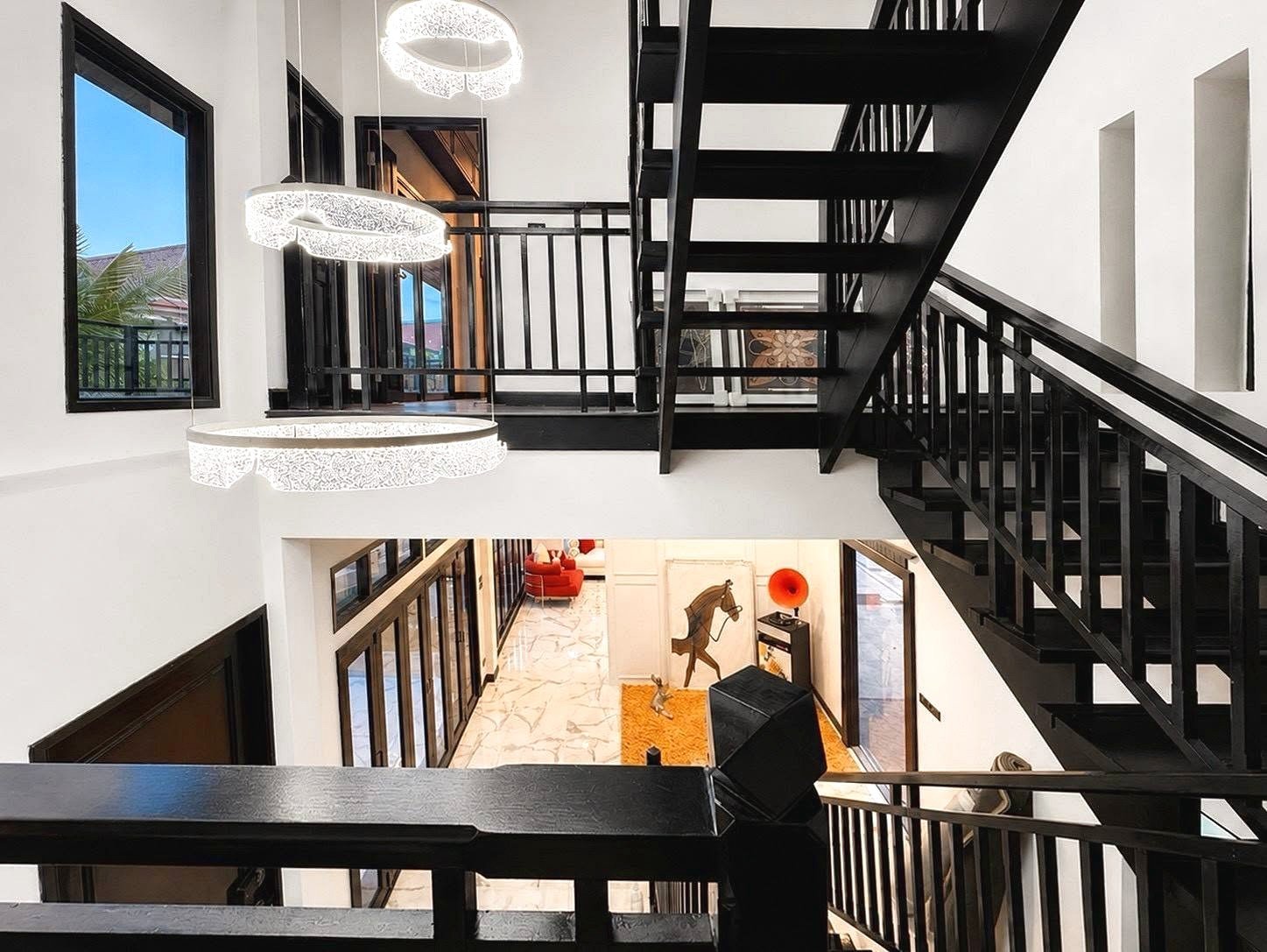 Dharawadi_Poolvilla_Rent_Rdl353_40 Interior view of a modern multi-level foyer with a black metal staircase, white walls, and circular pendant lights above.