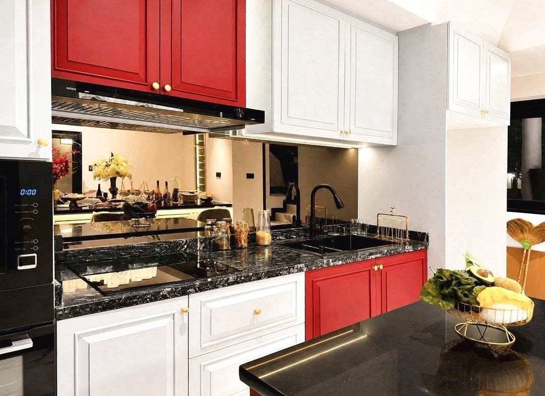 Modern kitchen with white lower cabinets, red upper cabinets, and black marble countertops surrounding a black sink and faucet on the right.