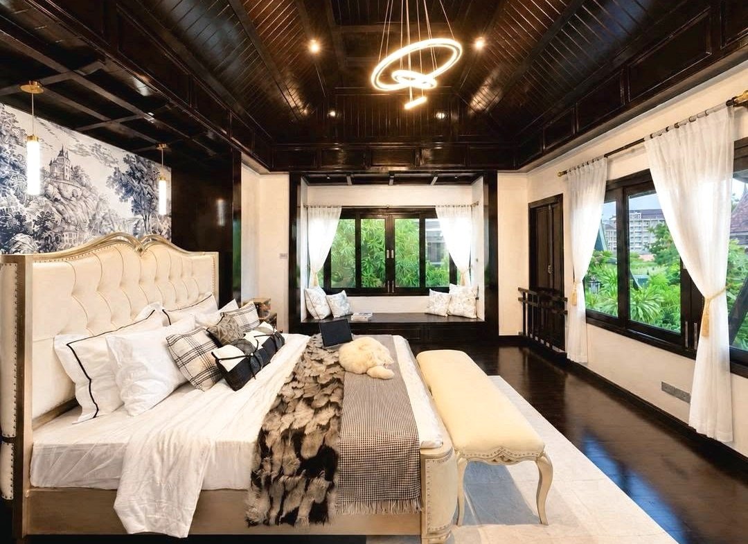 Luxurious bedroom with a cream tufted bed, white linens, and a fur throw beneath a circular neon chandelier in a dark wood–paneled room.