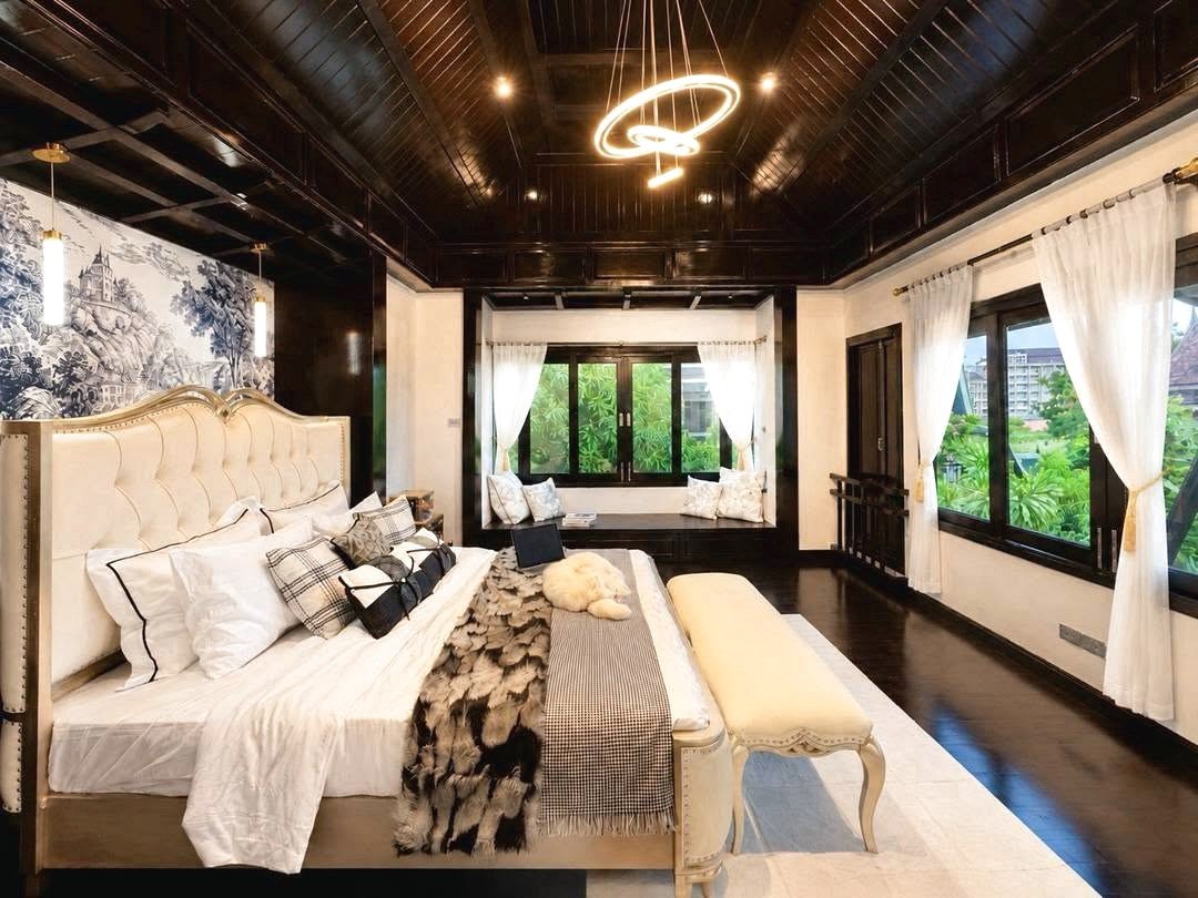 Dharawadi_Poolvilla_Rent_Rdl353_8 Luxurious bedroom with a cream tufted bed, white linens, and a fur throw beneath a circular neon chandelier in a dark wood–paneled room.