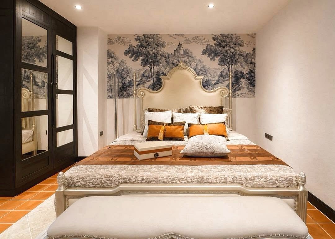 Elegant bedroom with an ornate upholstered headboard, nature mural and warm orange-accent pillows on the bed.