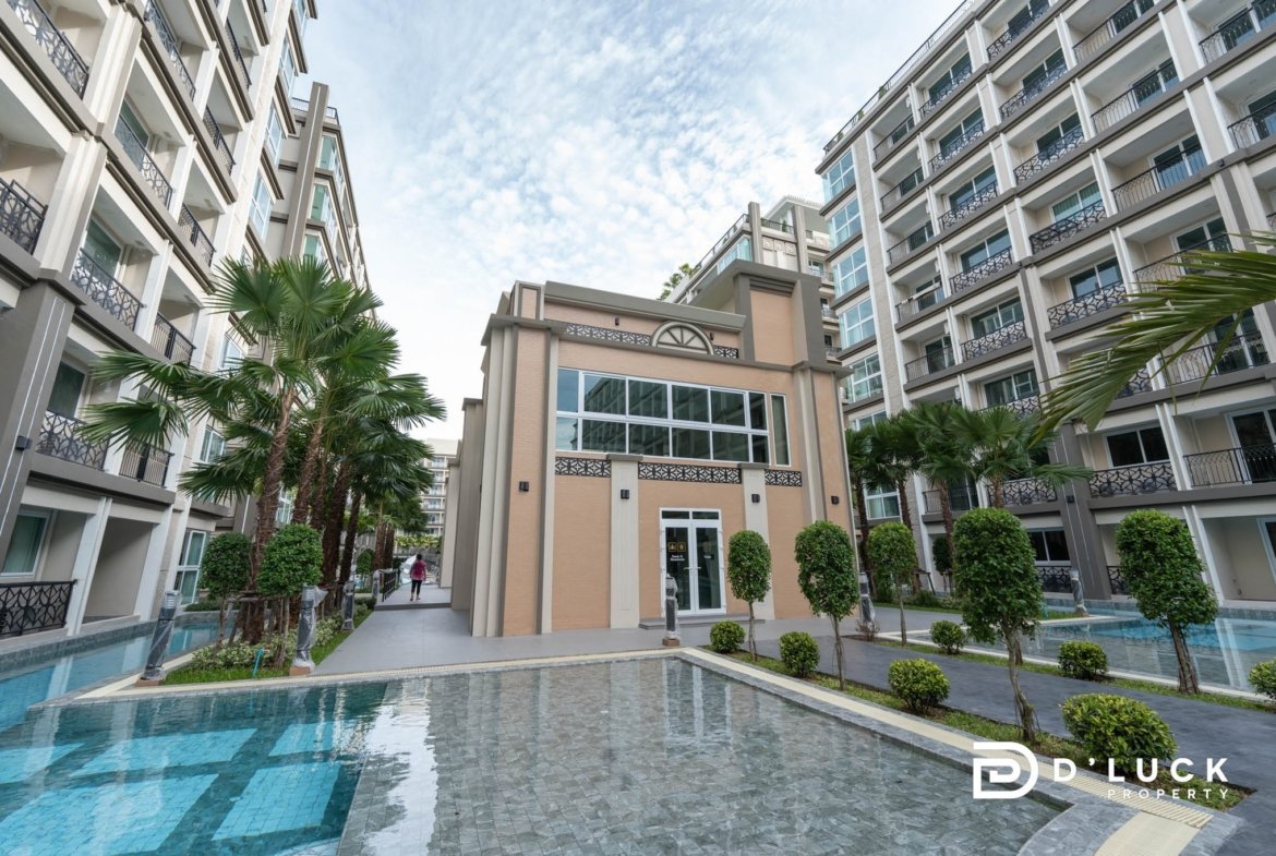 Modern apartment courtyard with beige buildings, balconies, and palm trees surrounding a shallow, reflective pool.