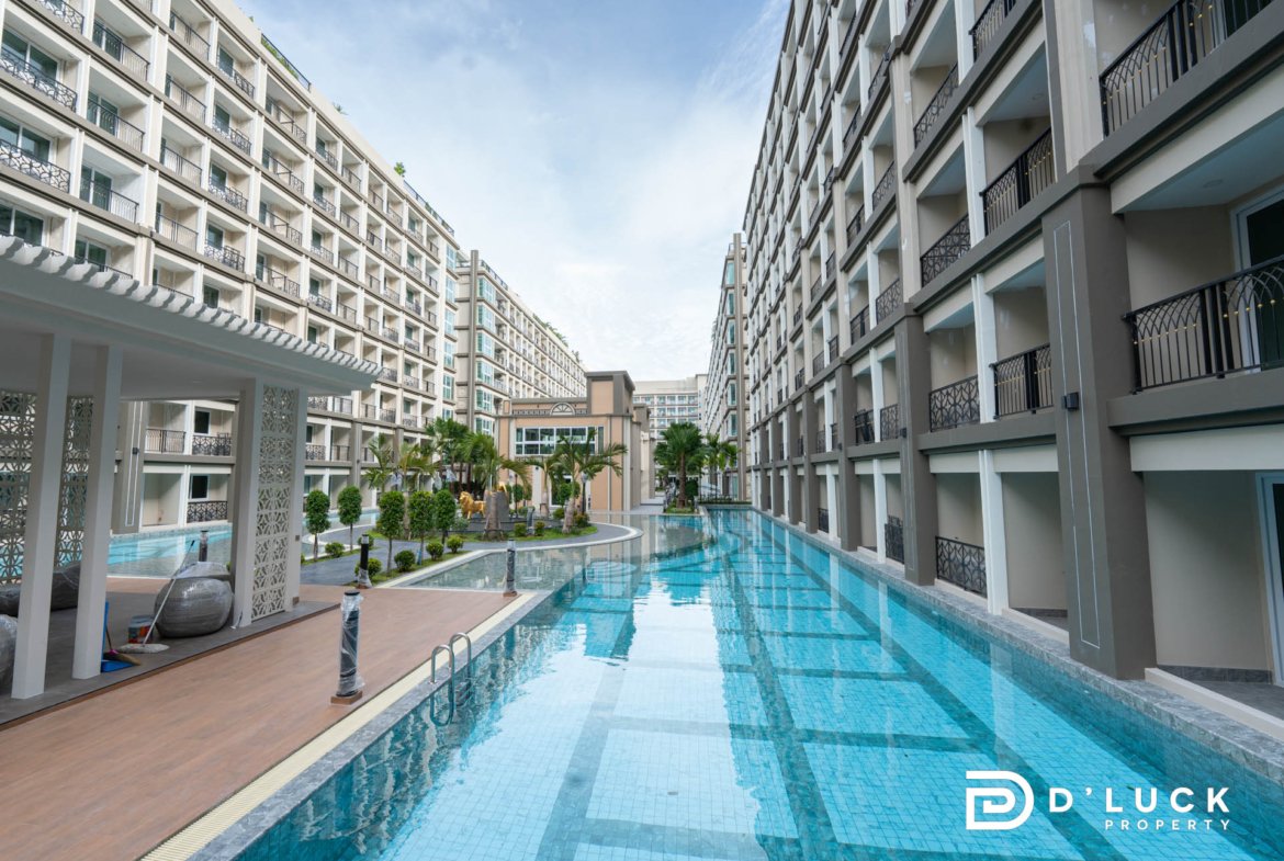 Modern residential complex with a long rectangular pool between high-rise buildings and balconies on both sides.
