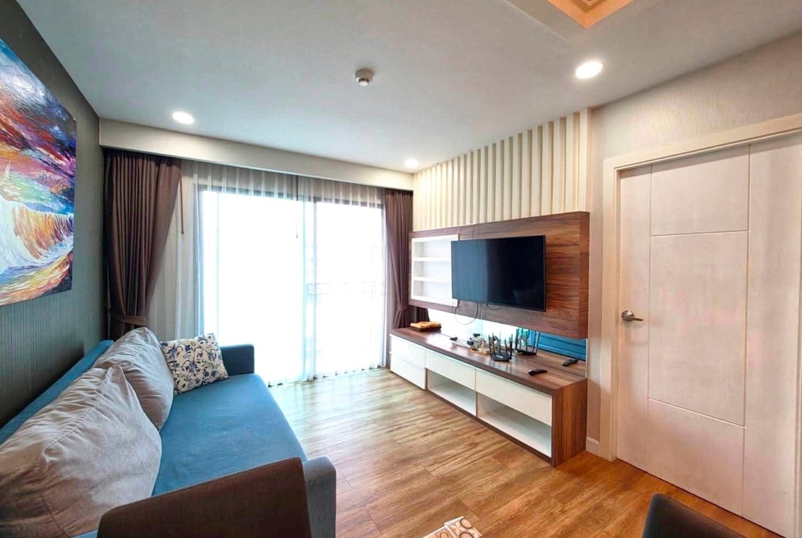 Bright living room with a blue sofa, colorful wall art, and a wood TV wall unit.