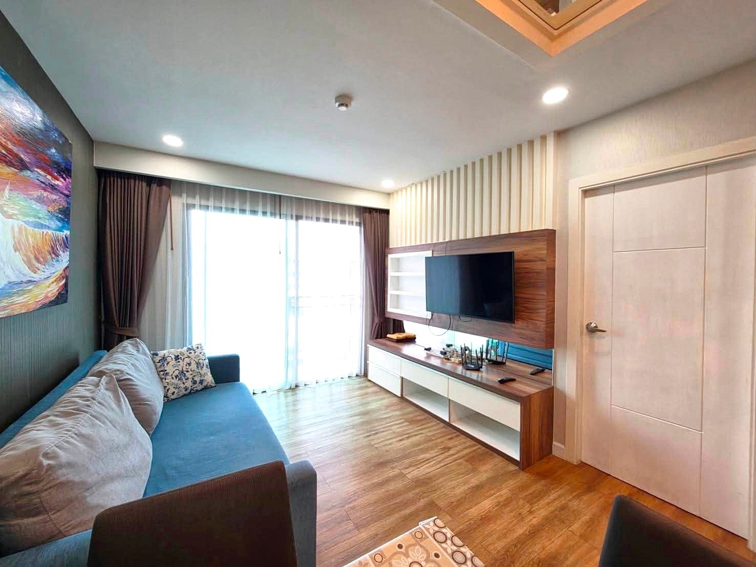 Dusit_1_2BR_Rent_Rdl279 Bright living room with a blue sofa, colorful wall art, and a wood TV wall unit.