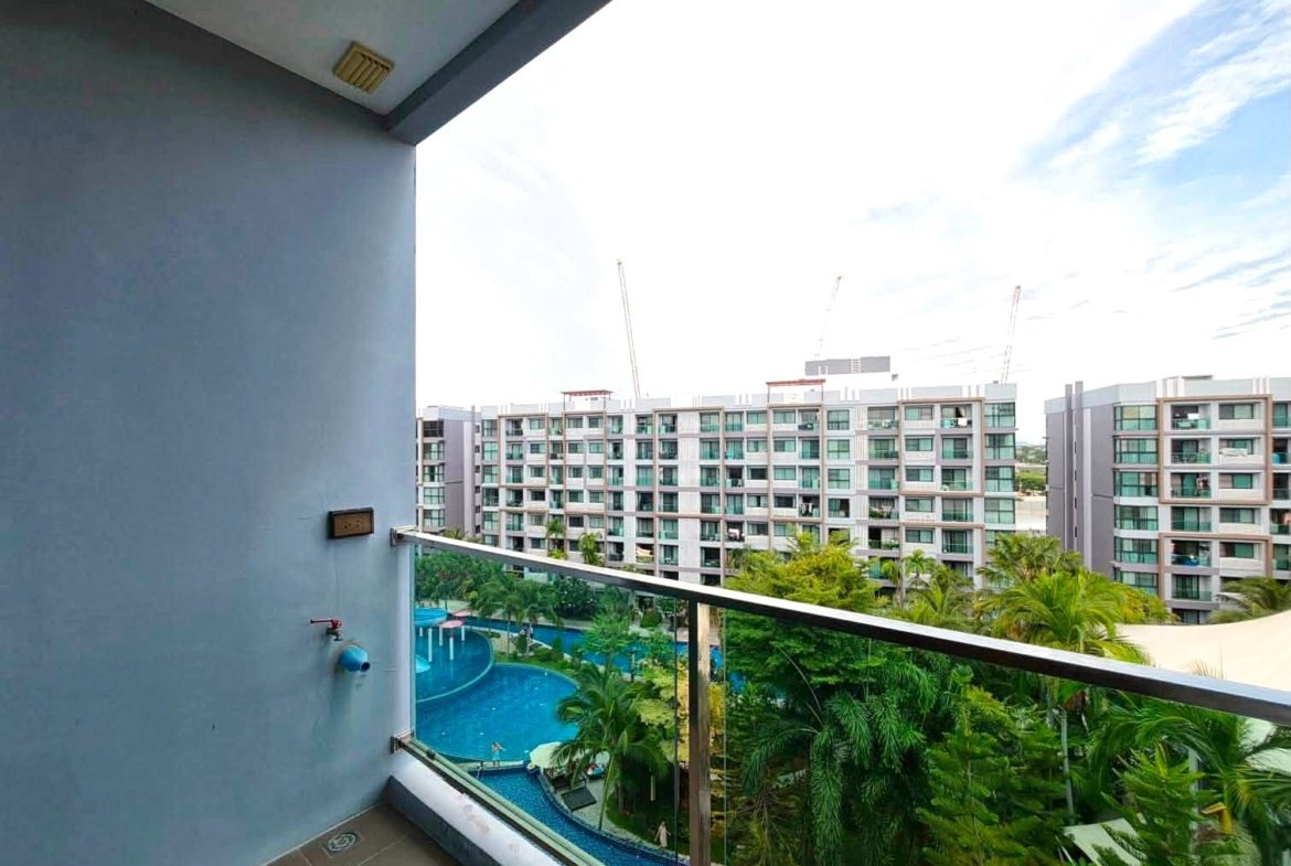 Balcony view overlooking a pool area with palm trees and a row of modern white apartment buildings in the background.