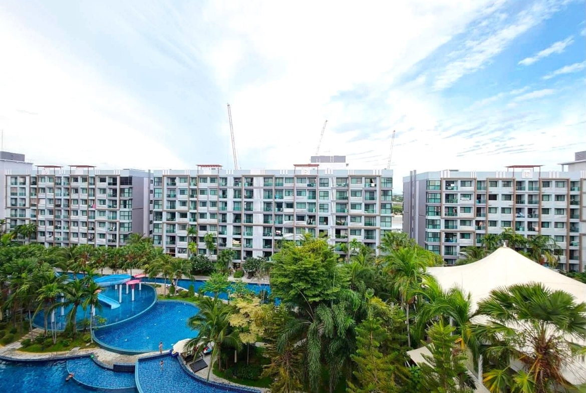 View of a resort complex with multiple low-rise buildings surrounding a winding blue pool and palm trees