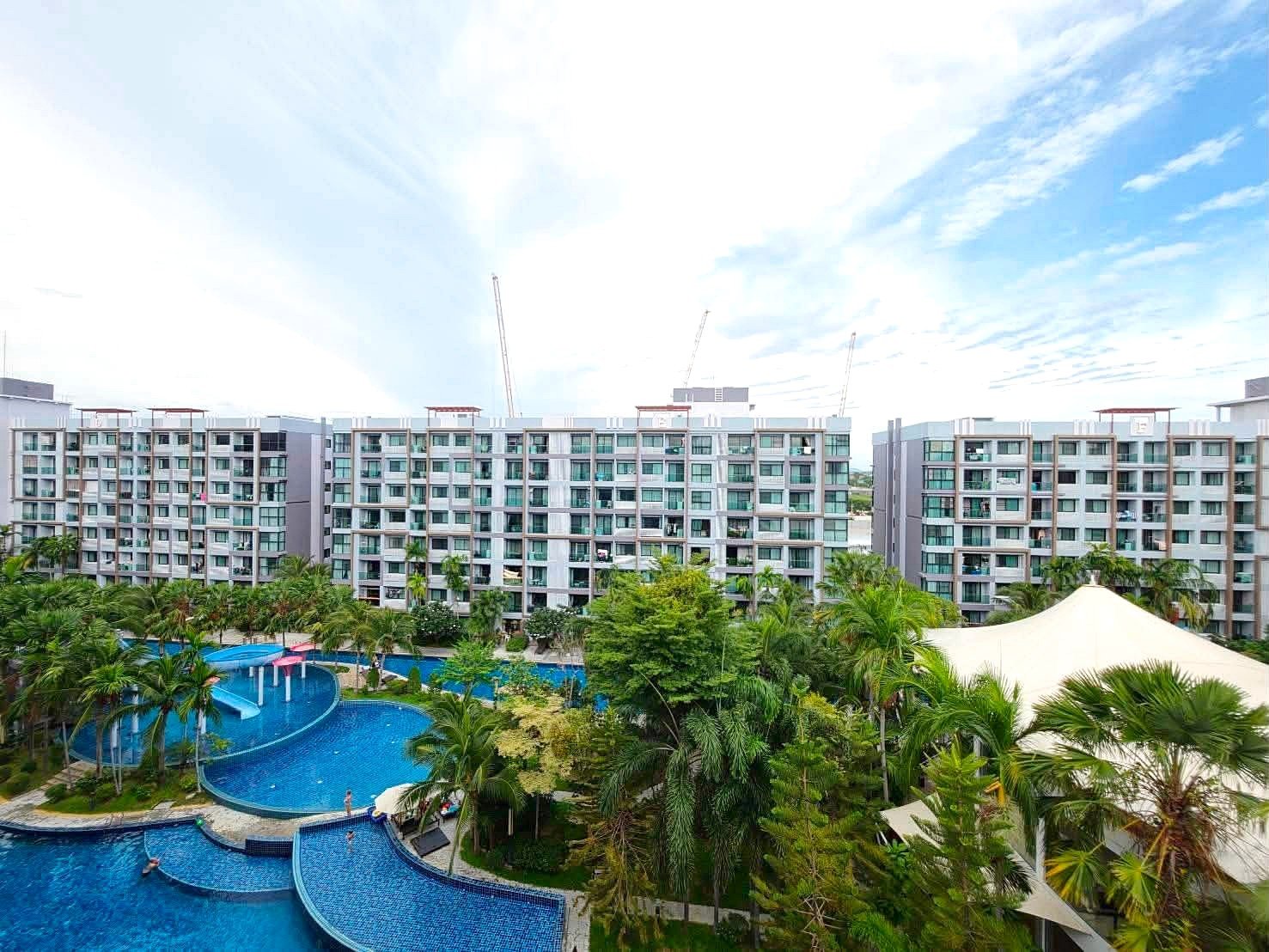Dusit_1_2BR_Rent_Rdl279_17 View of a resort complex with multiple low-rise buildings surrounding a winding blue pool and palm trees