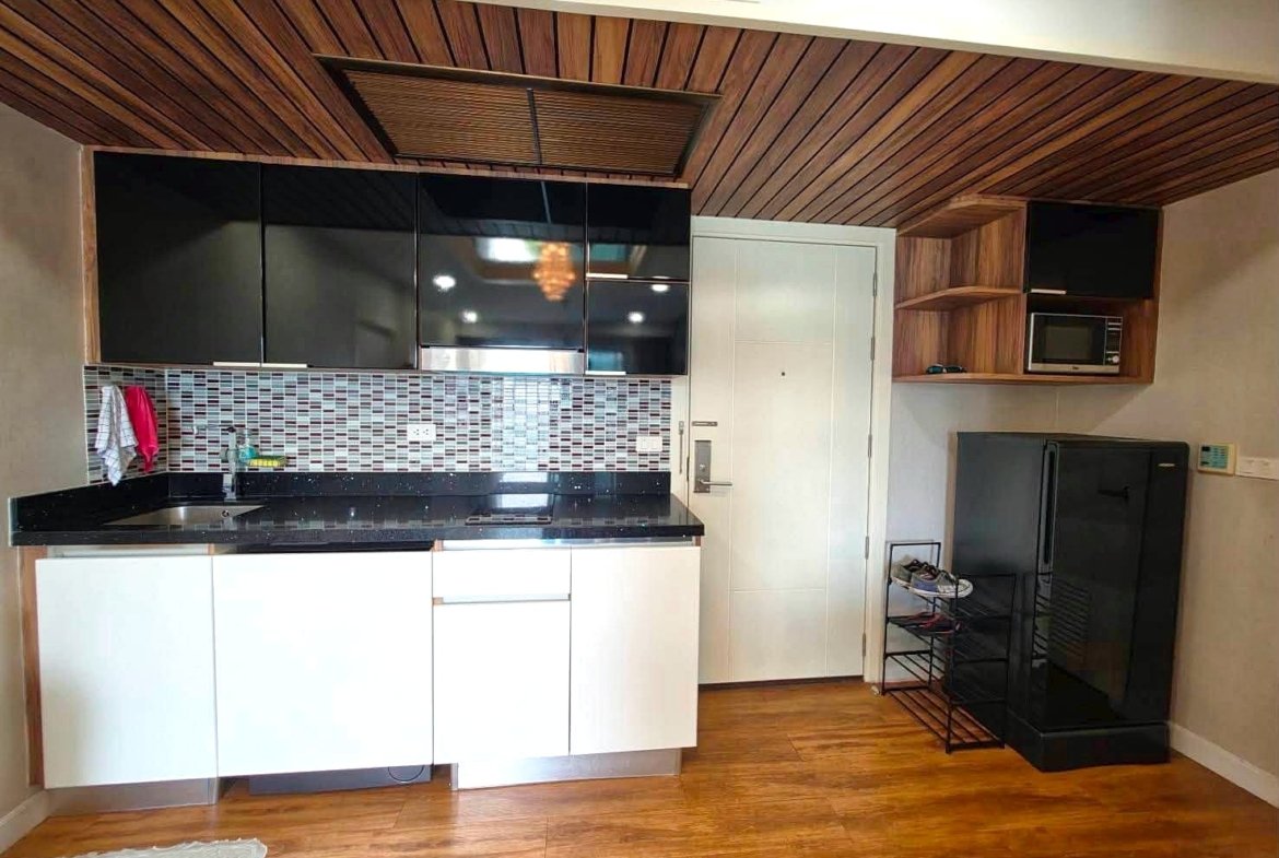Modern kitchen with black countertops, white cabinets, and a mosaic tile backsplash under a wooden slat ceiling.