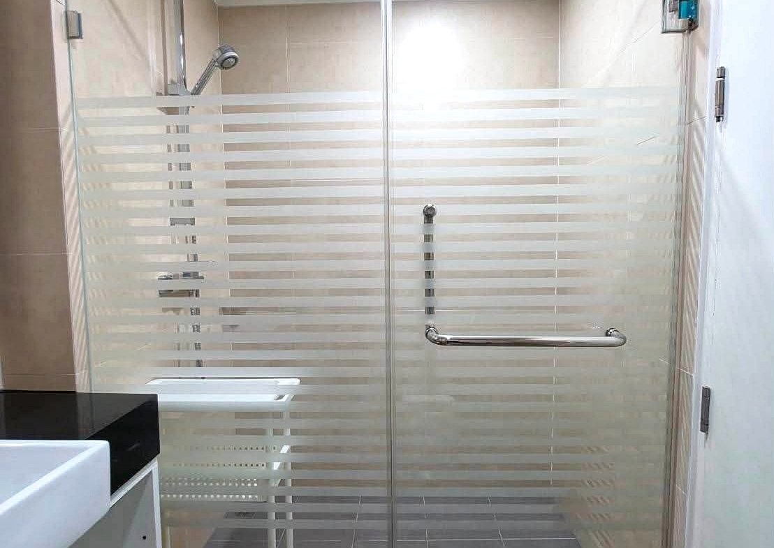 Glass shower door with frosted horizontal stripes and chrome handle in a beige-tiled bathroom