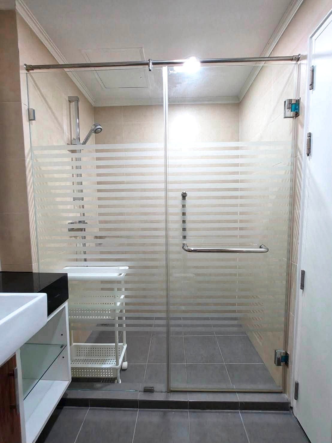 Dusit_1_2BR_Rent_Rdl279_8 Glass shower door with frosted horizontal stripes and chrome handle in a beige-tiled bathroom