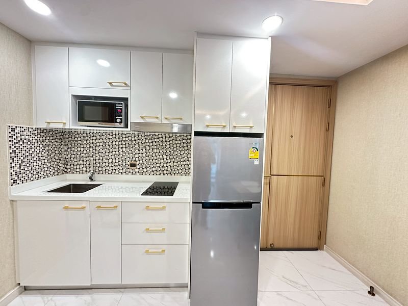 Modern white kitchen with mosaic tile backsplash, stainless fridge, sink, and microwave above the counter.
