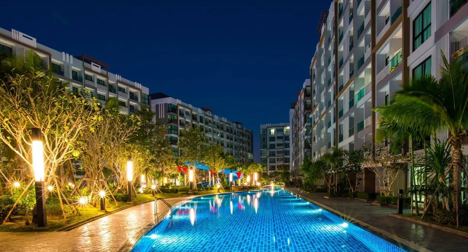 Nighttime view of a glowing blue pool flanked by modern apartment buildings and palm trees.