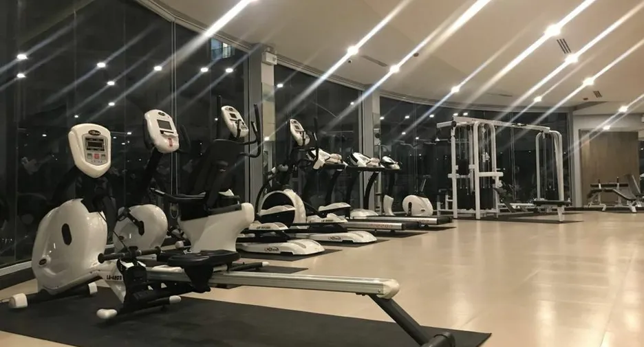 Row of cardio machines in a modern gym, including stationary bikes and treadmills, with a glass wall and bright overhead lights.