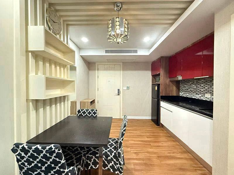 Modern dining table with black surface and four black-and-white patterned chairs in a kitchen, with white wall shelves on the left and red upper cabinets on the right.