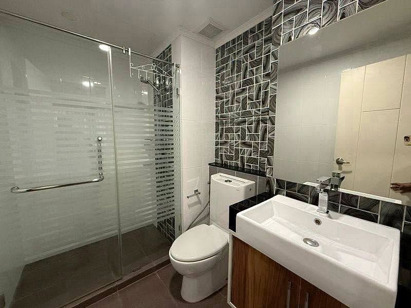 Modern bathroom with glass shower enclosure, toilet, and rectangular sink with wooden cabinet beneath.
