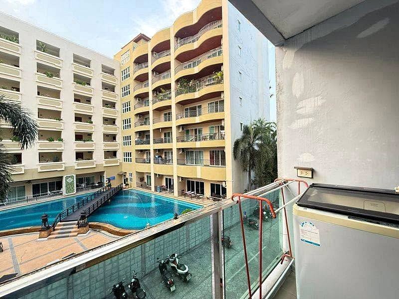 Residential complex courtyard with a large blue swimming pool surrounded by multi-story beige buildings and balconies.