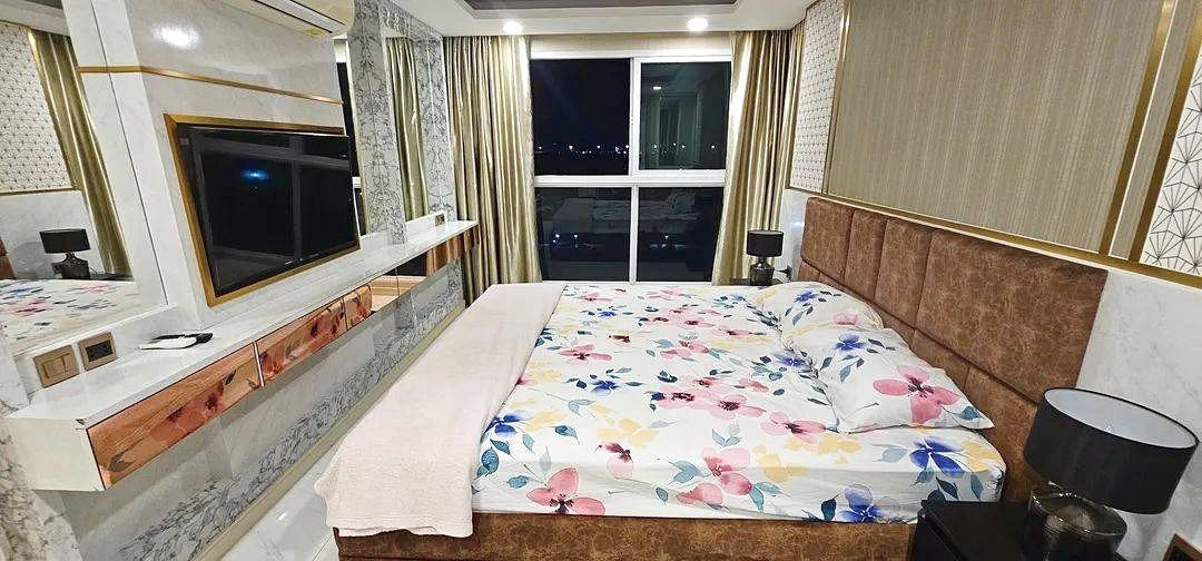 Luxurious hotel bedroom with a flower-patterned bedspread, brown upholstered headboard, marble surfaces, and a large window at night.