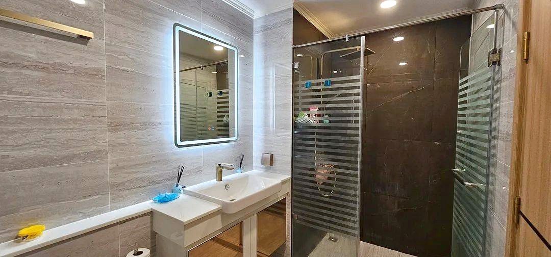 Bright modern bathroom with a white rectangular sink, backlit mirror, and a glass shower enclosure with frosted stripes.