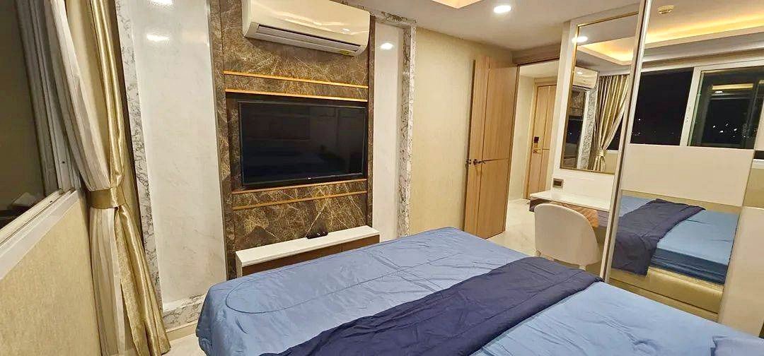 Modern hotel room with a wall-mounted TV, marble accent wall, and blue bedding.