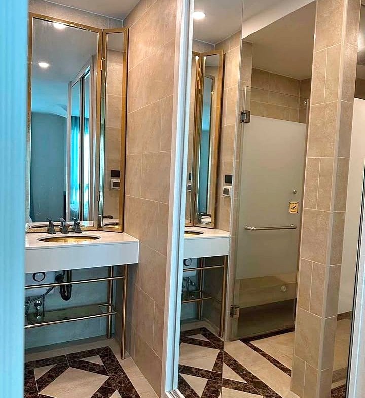 Public bathroom with beige tile walls, a double sink and mirrors, and a frosted glass stall door; geometric tiled floor.