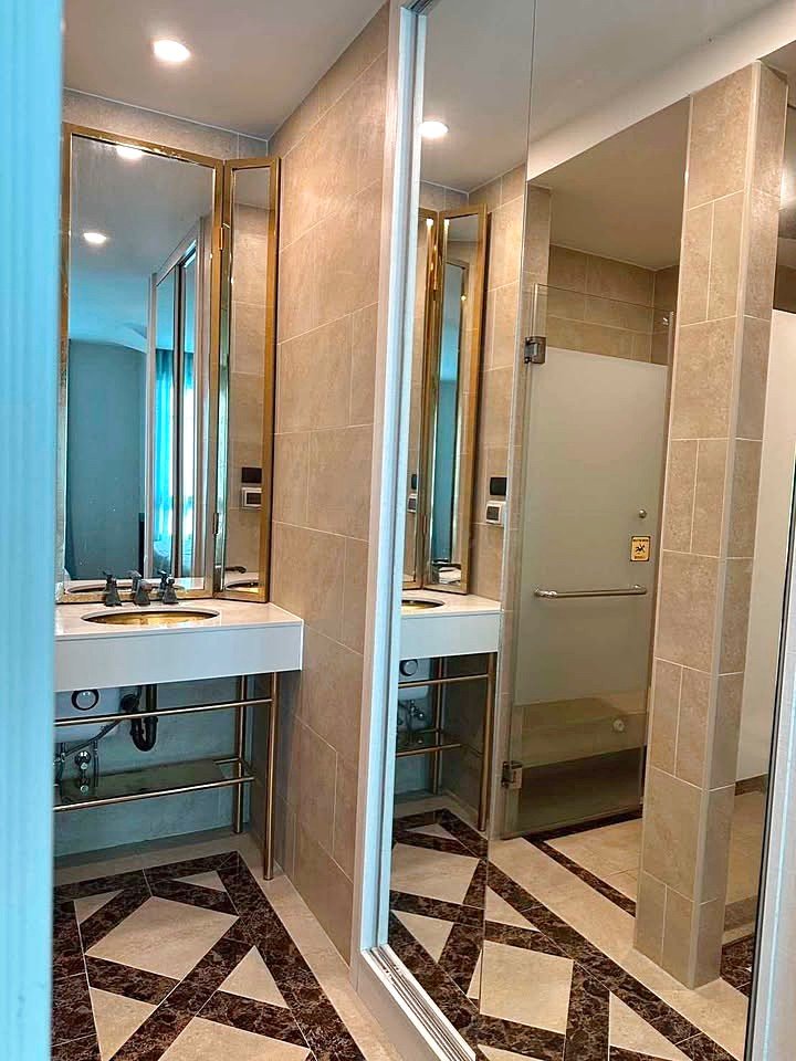 Espana_Condo_2BR_G517_518_10 Public bathroom with beige tile walls, a double sink and mirrors, and a frosted glass stall door; geometric tiled floor.