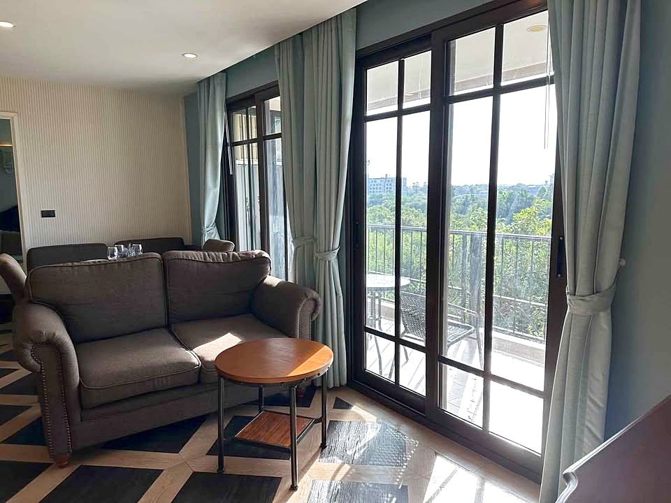 Living room with a gray sofa, round wooden coffee table, and large glass doors opening to a sunlit balcony.
