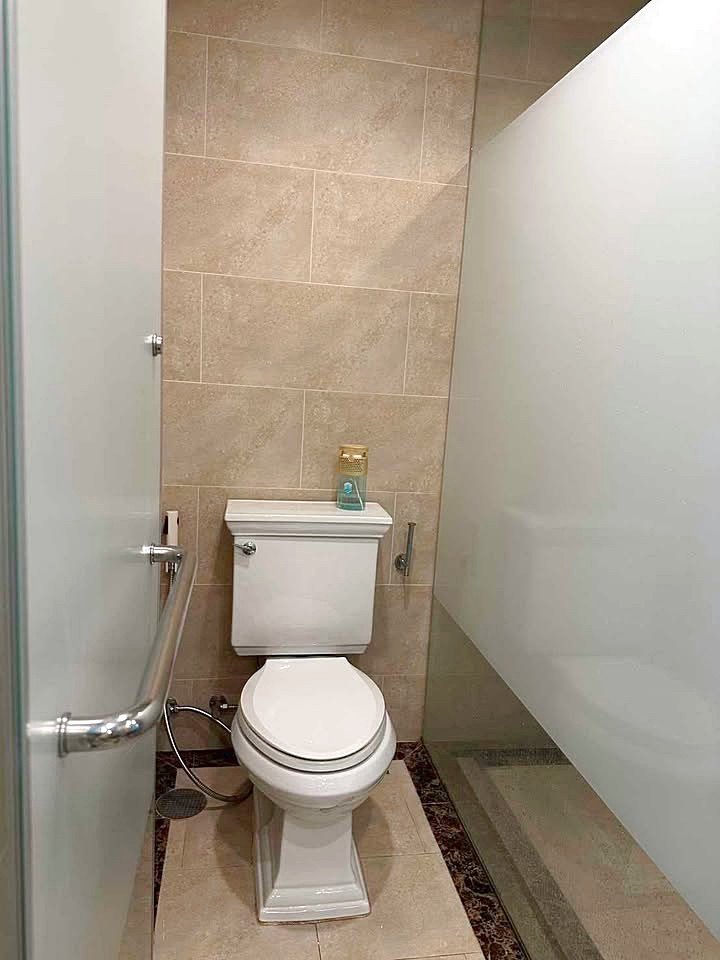 Espana_Condo_2BR_G517_518_5 Toilet in a small tiled bathroom with a glass shower wall to the right and a chrome grab bar on the door side; a small blue bottle sits on the toilet tank.