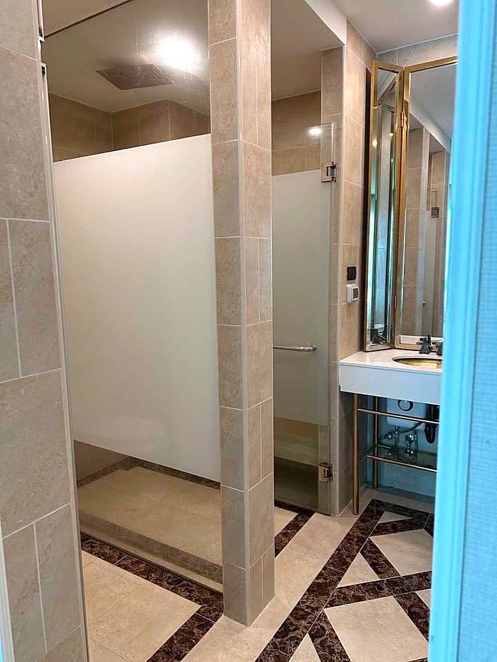 Espana_Condo_2BR_G517_518_6 Public bathroom interior with frosted shower stalls, beige tiles, and a vanity with mirror on the right.