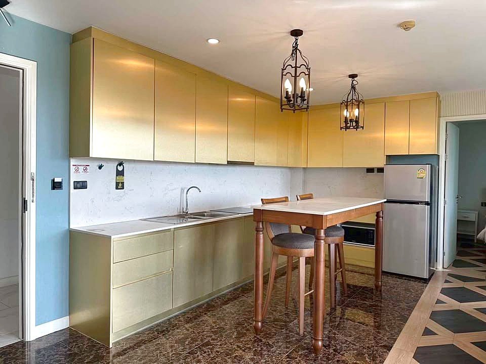 Golden kitchen with long upper and lower cabinets, marble backsplash, and a wooden island with two stools.