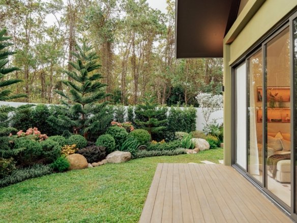 Modern house with large glass sliding doors opening to a wooden deck and lush garden.