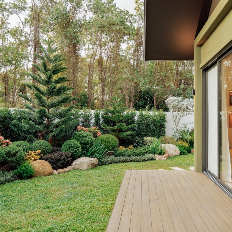 Modern house with large glass sliding doors opening to a wooden deck and lush garden