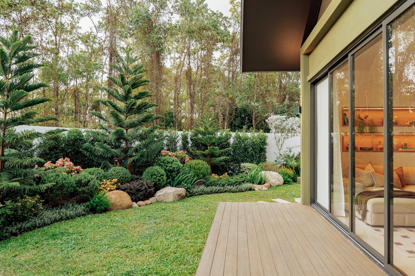 Modern house with large glass sliding doors opening to a wooden deck and lush garden.