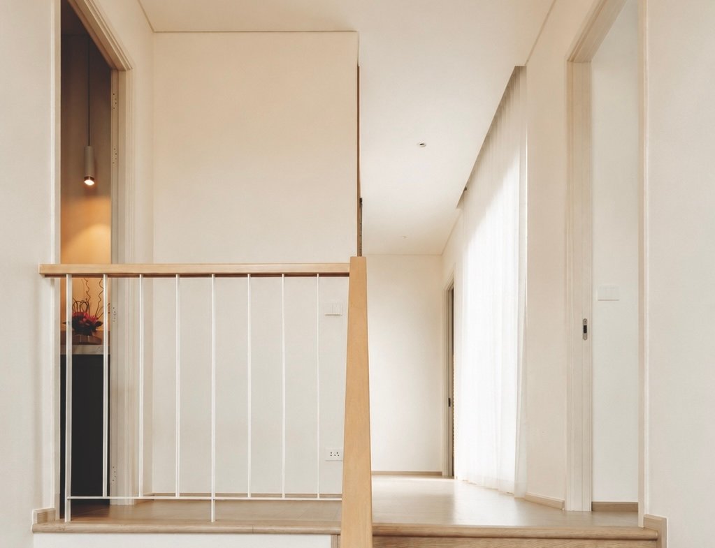 Wooden staircase with a light-wood handrail leading to a bright, minimalist hallway.