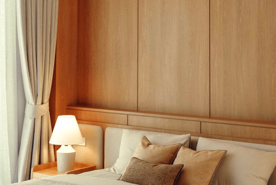 Hotel bedroom with a neatly made bed, beige bedding, and a wood-paneled headboard wall. A bedside lamp glows on a small wooden table.