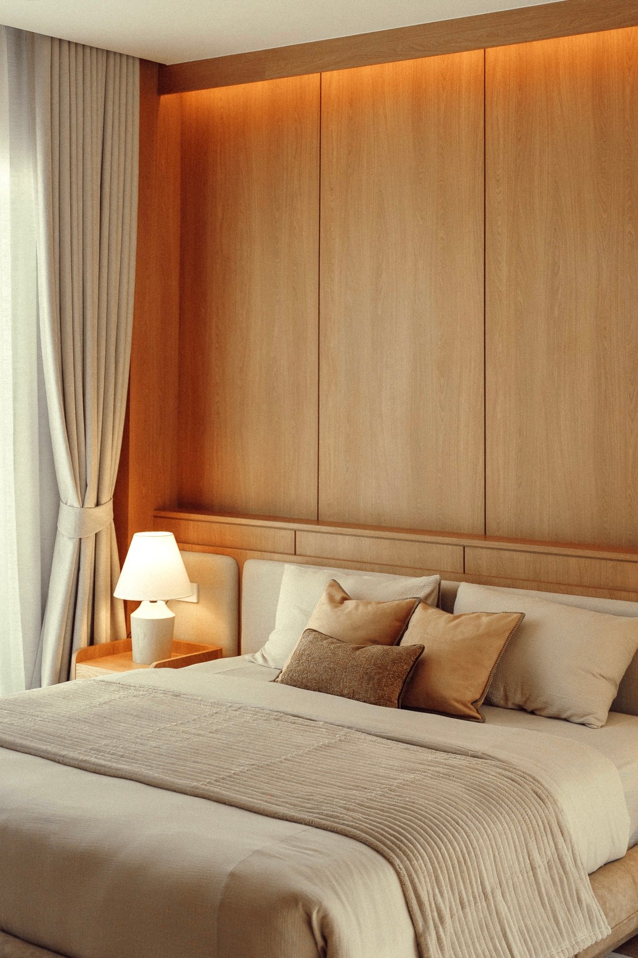 Hotel bedroom with a neatly made bed, beige bedding, and a wood-paneled headboard wall. A bedside lamp glows on a small wooden table.