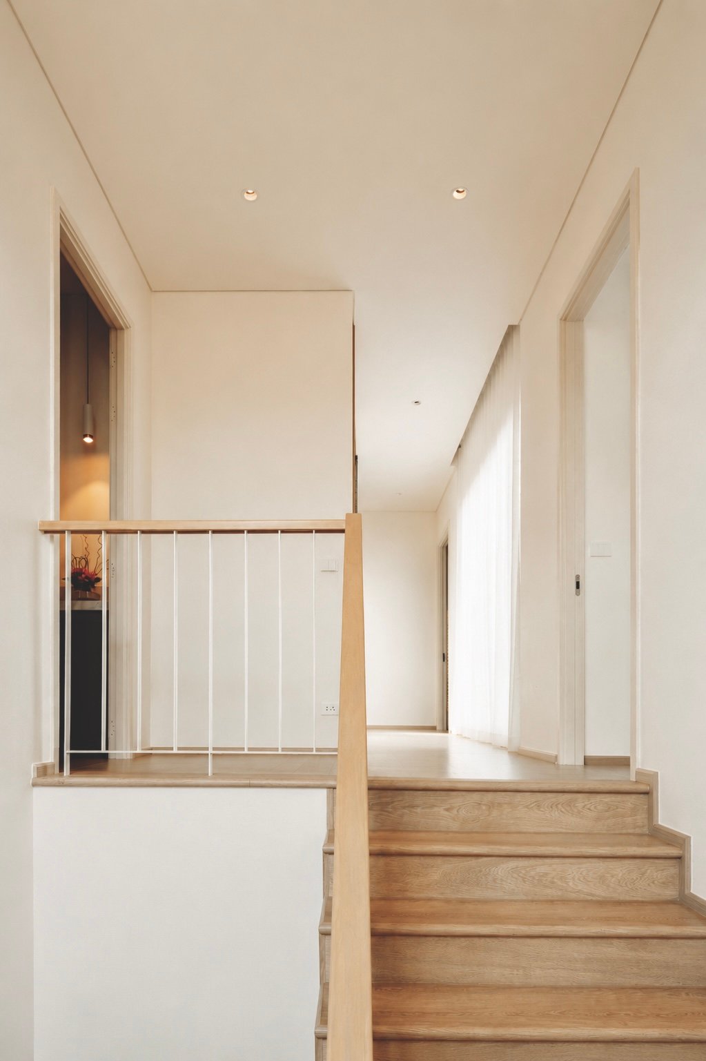 Wooden staircase with a light-wood handrail leading to a bright, minimalist hallway.